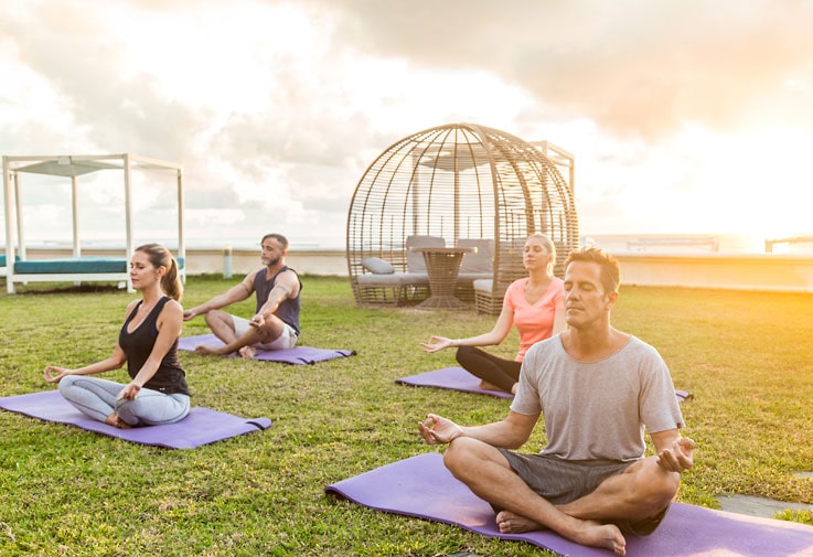 Vier Yogis meditieren auf Yogamatten im Sonnenuntergang